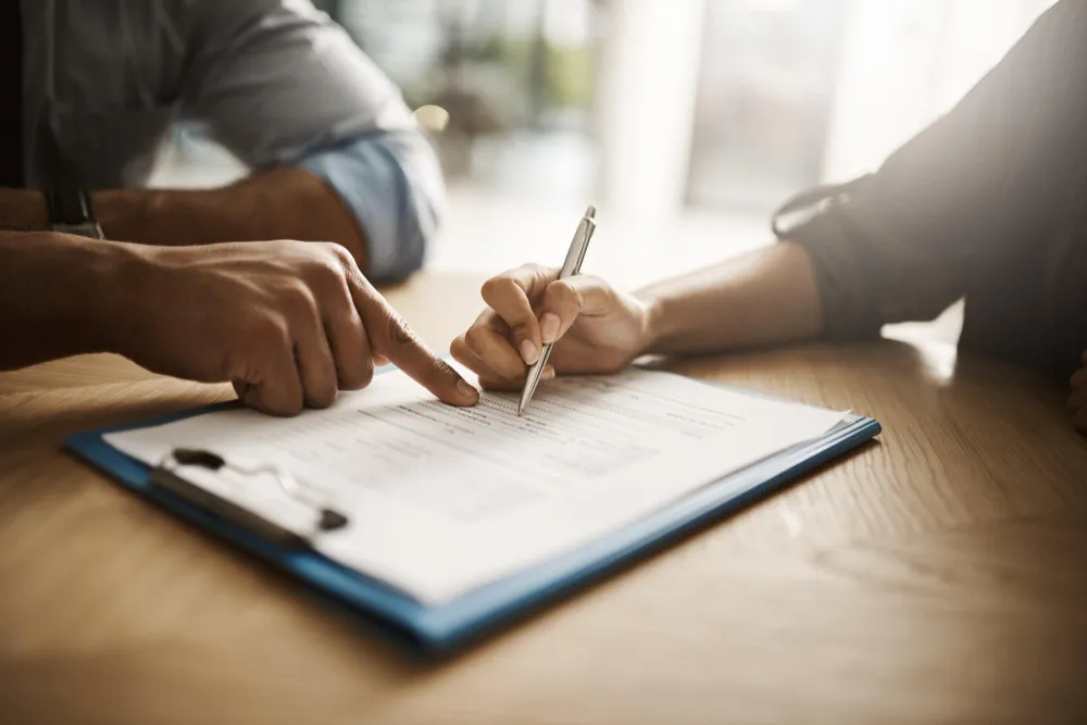 Mãos preenchendo documentos necessários para aposentadoria em uma mesa.