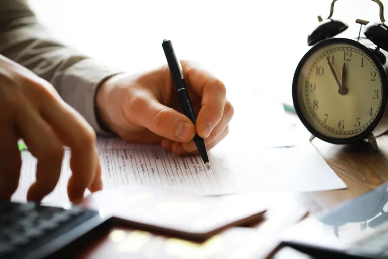 Mão escrevendo em formulário com relógio indicando tempo de contribuição mínimo para aposentadoria.