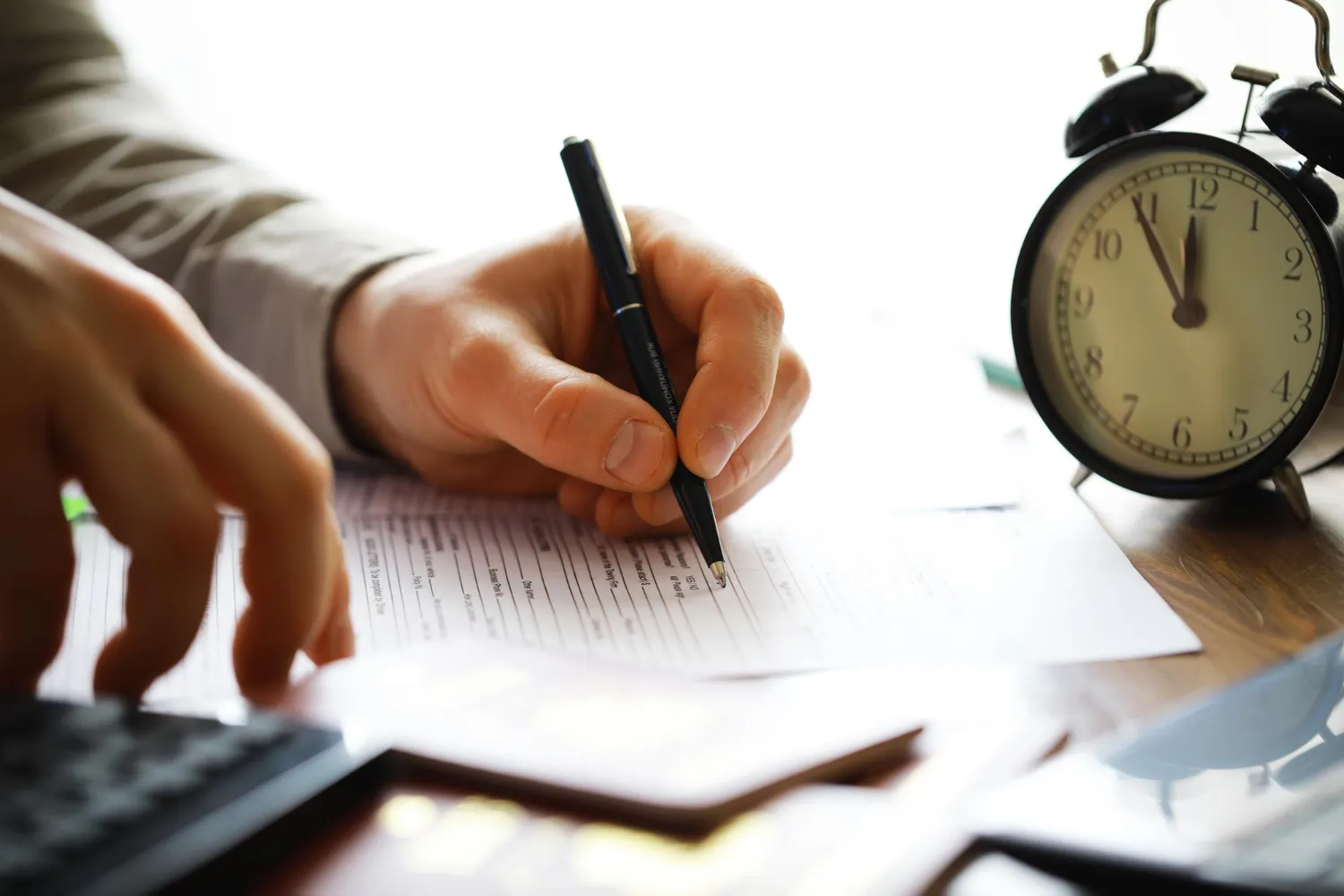 Mão escrevendo em formulário com relógio indicando tempo de contribuição mínimo para aposentadoria.